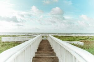 white boardwalk bridge extends out to the grassy seashore